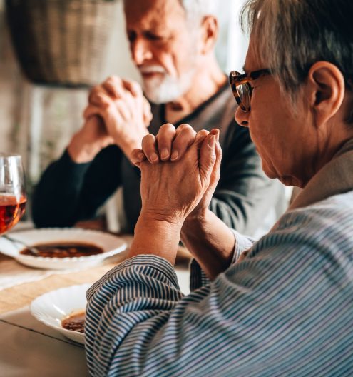 Christian senior couple praying at table worshipping the Lord