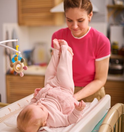 Mother changes baby girl on changing table in cozy nursery
